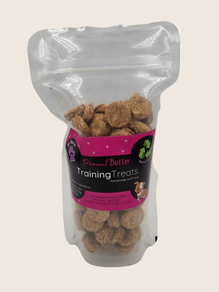 A clear plastic pouch filled with peanut butter training treats for dogs. The pouch has a pink label with product details.